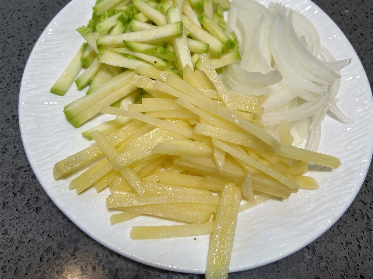 Strisce sottili di zucchina, cipolla e patata su un piatto bianco.