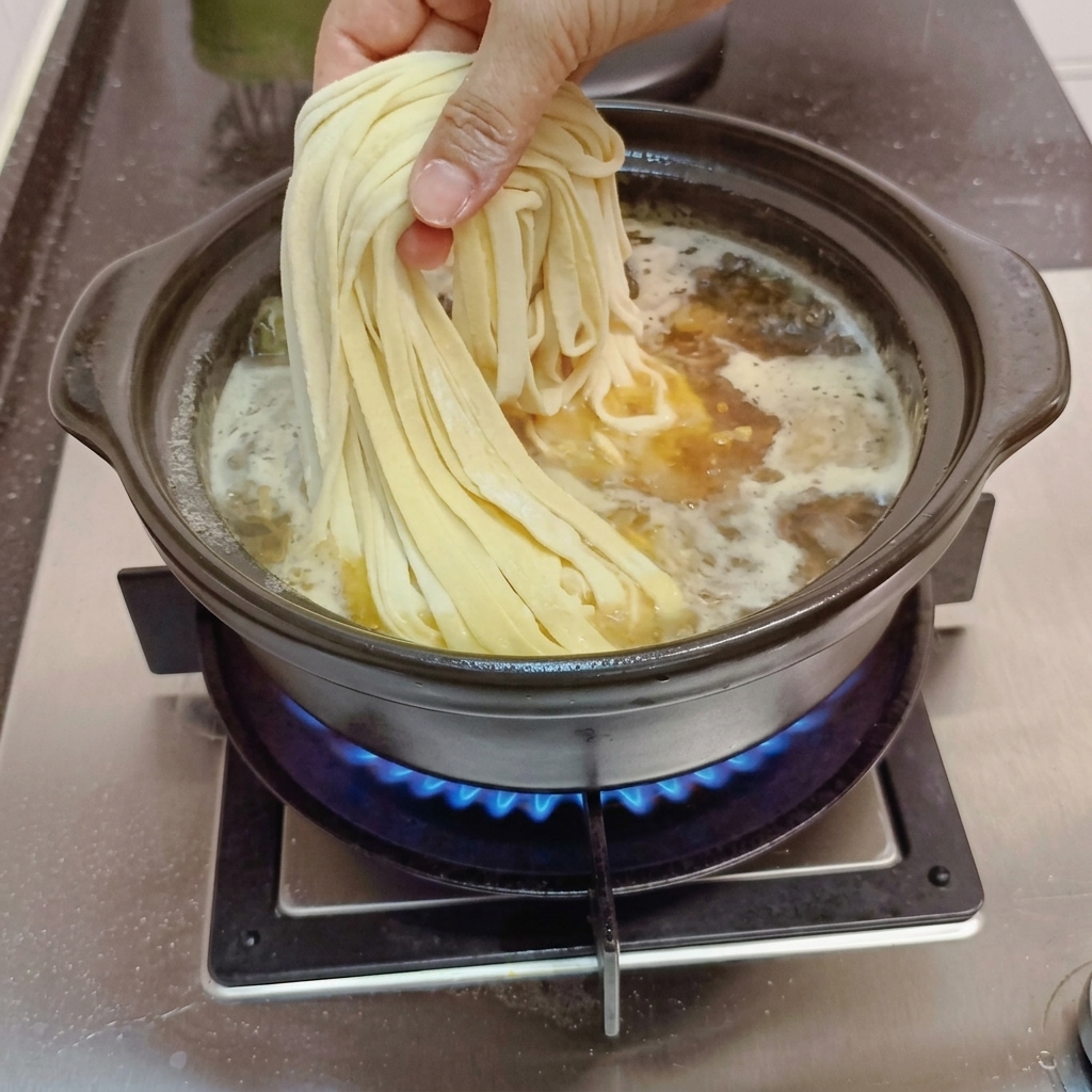 Noodle fatti a mano calati nel brodo in ebollizione.