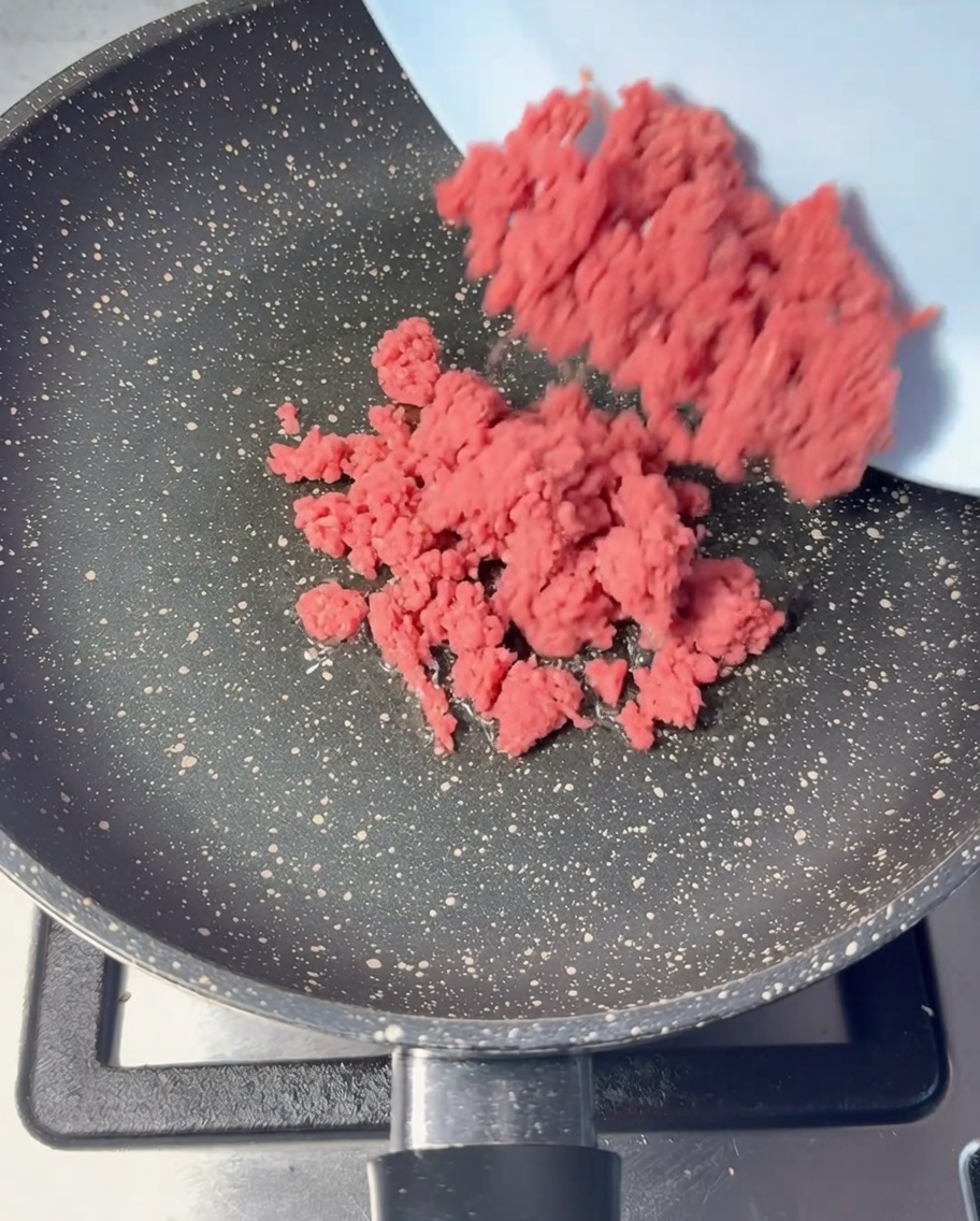 Carne macinata cruda aggiunta in una padella oliata.