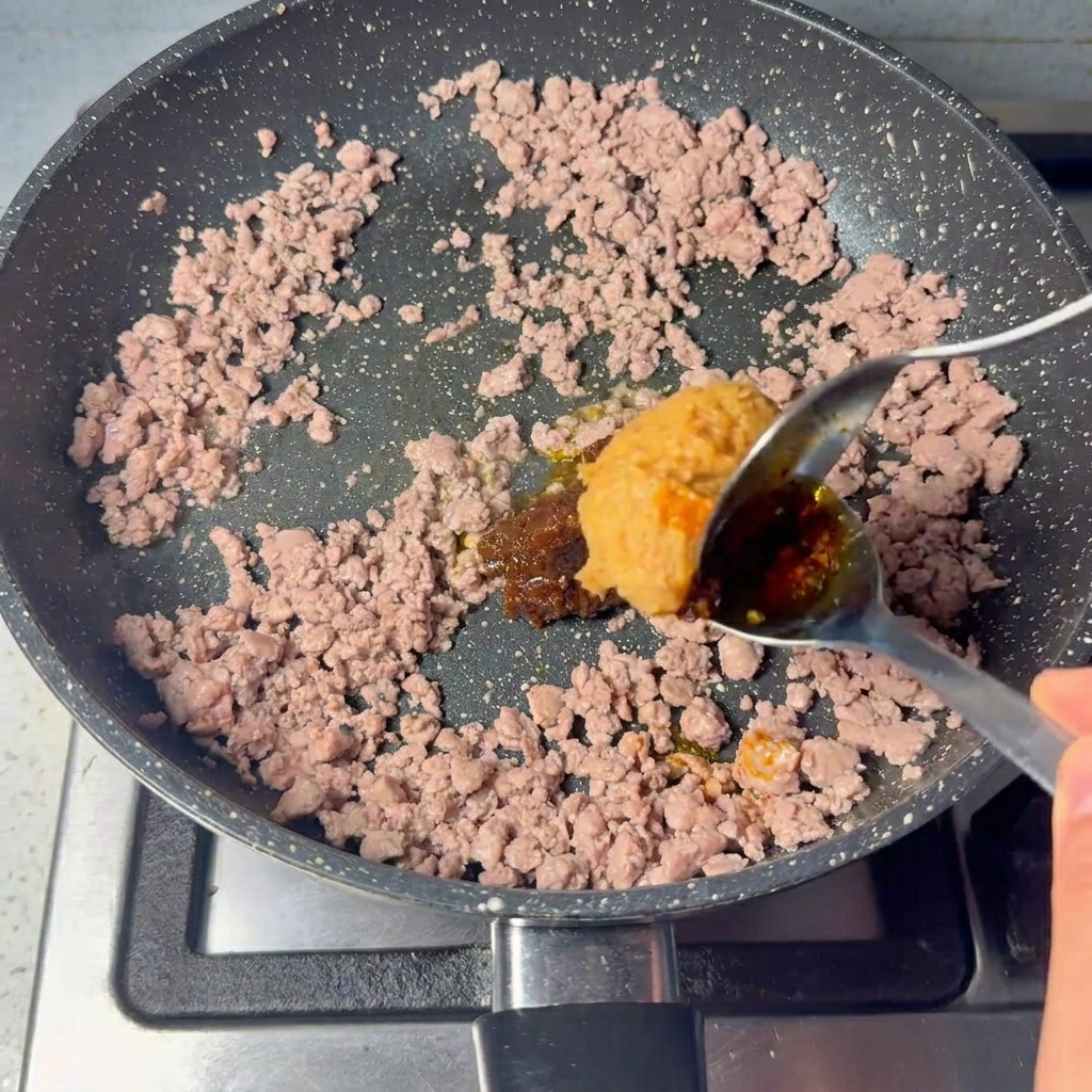 Un grosso cucchiaio di pasta marrone e densa mescolato alla carne macinata cotta.