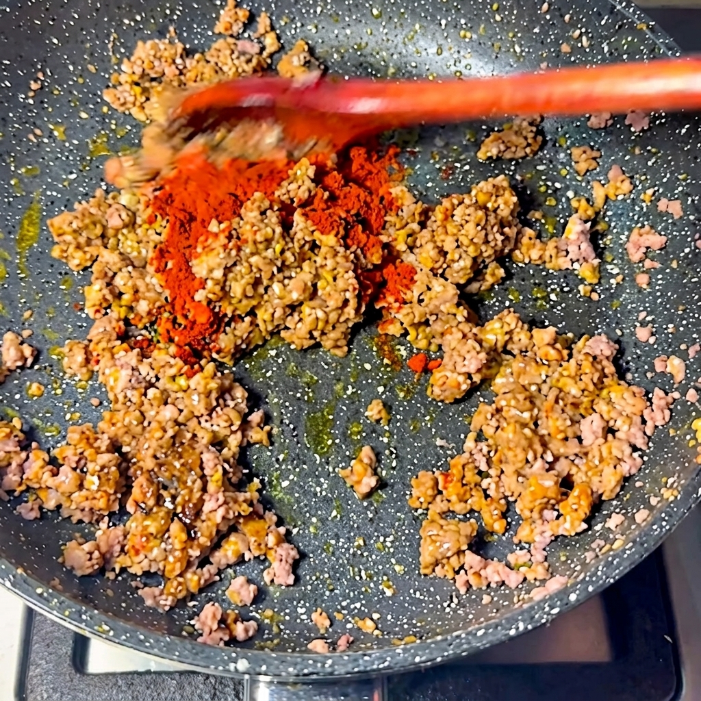 Peperoncino rosso brillante in polvere cosparso sulla miscela di carne in padella.
