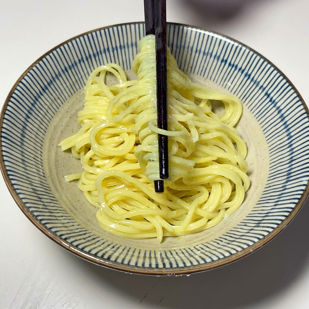 Noodles gialli cotti adagiati in una ciotola di ceramica con le bacchette.