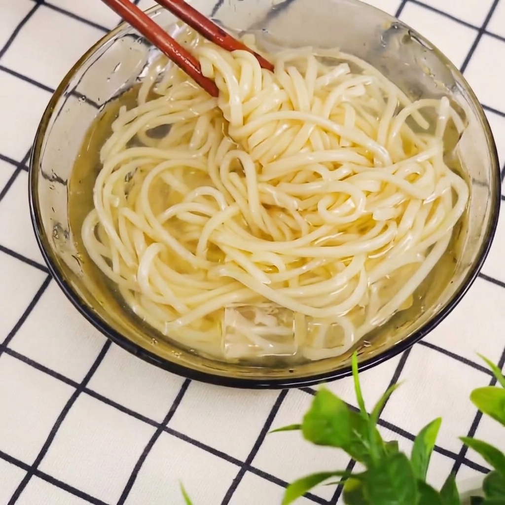 Noodles cotti sollevati da una pentola con le bacchette.