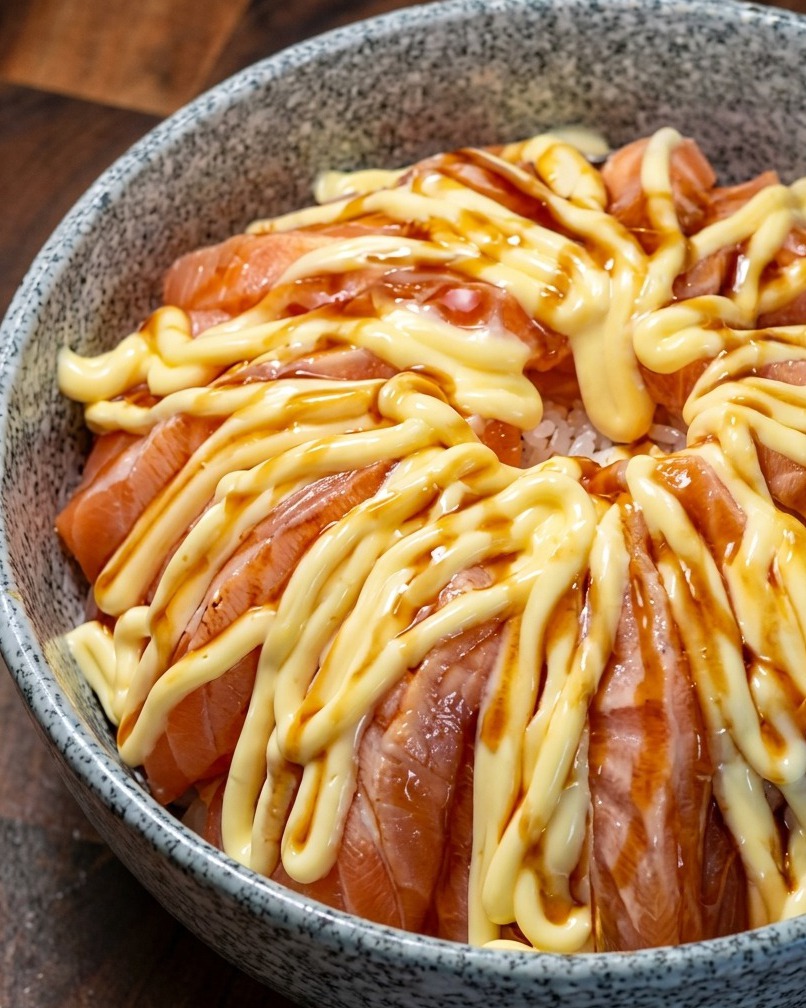 Un bowl di salmone condito con salsa teriyaki scura sopra lo strato di maionese.