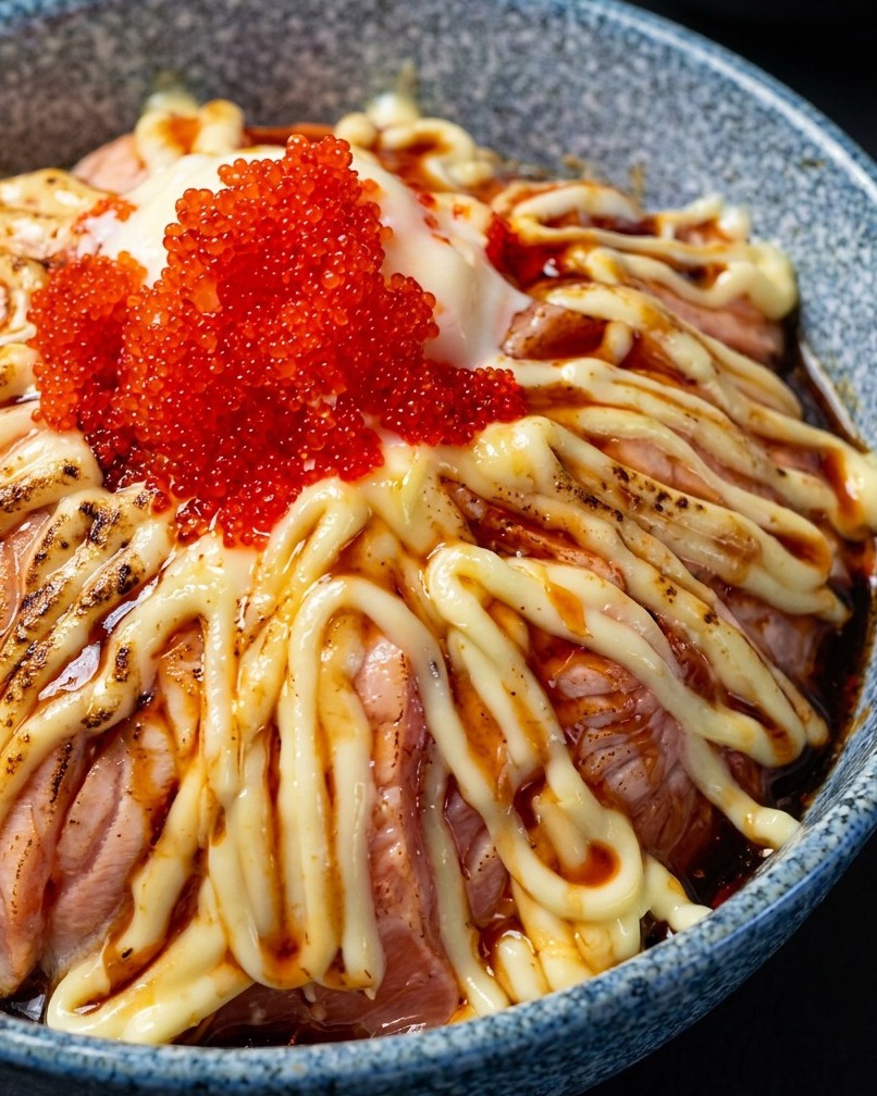 Cannello che scotta leggermente la superficie di un bowl di salmone guarnito con maionese e uova di pesce.