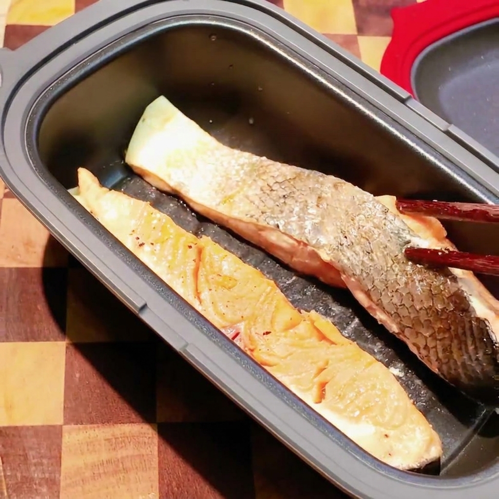 Bacchette girano un filetto di salmone parzialmente cotto allinterno di una padella scura da microonde.
