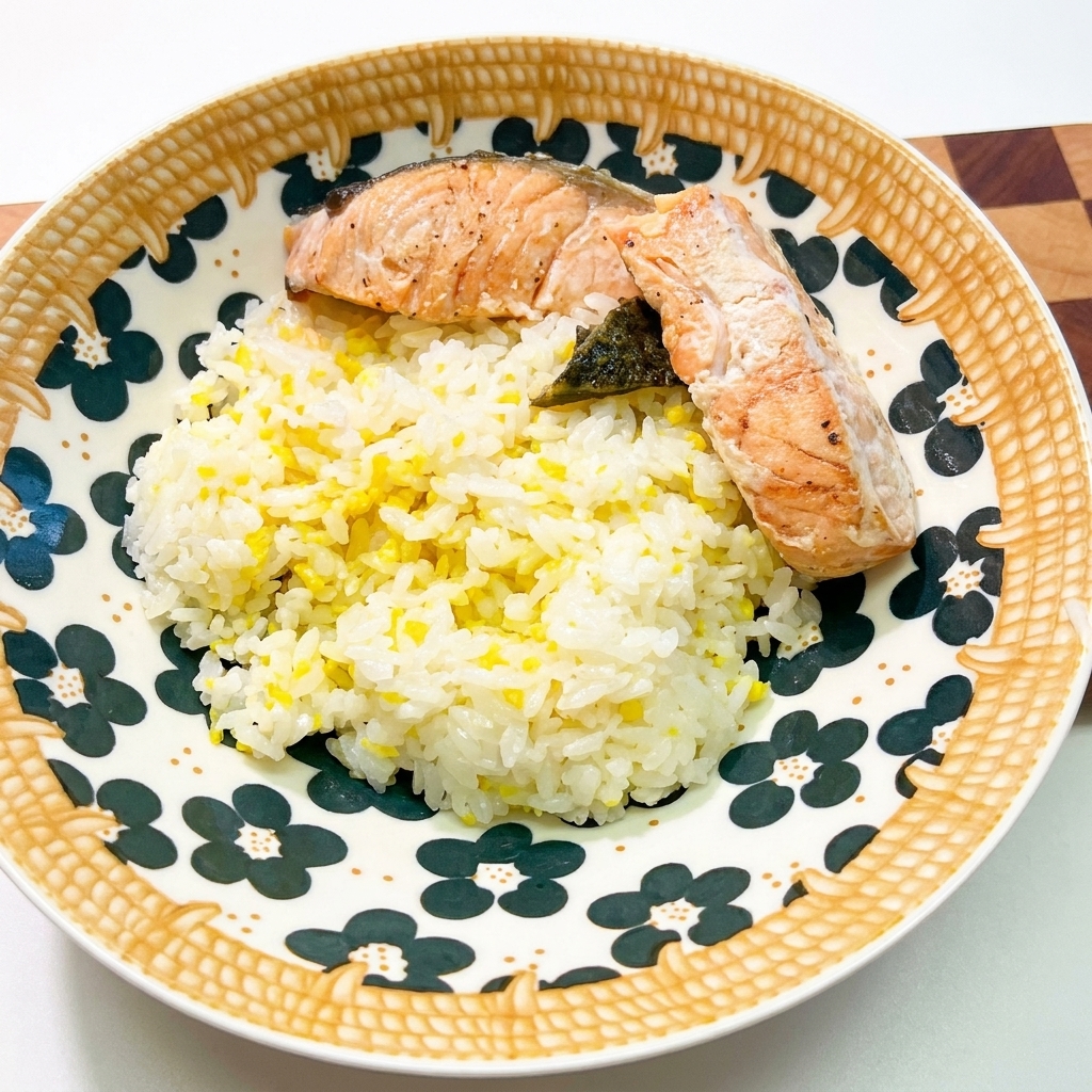 Una ciotola di ceramica decorata riempita con riso bianco, completata da due pezzi di salmone cotto e alghe scure.