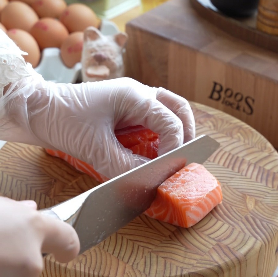 Spessi cubetti di salmone fresco crudo preparati con cura su un tagliere di legno.