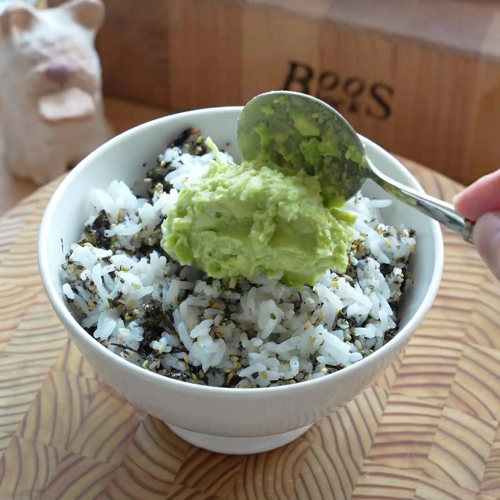 Uno strato di crema di avocado steso uniformemente sopra la base di riso in una ciotola da portata.