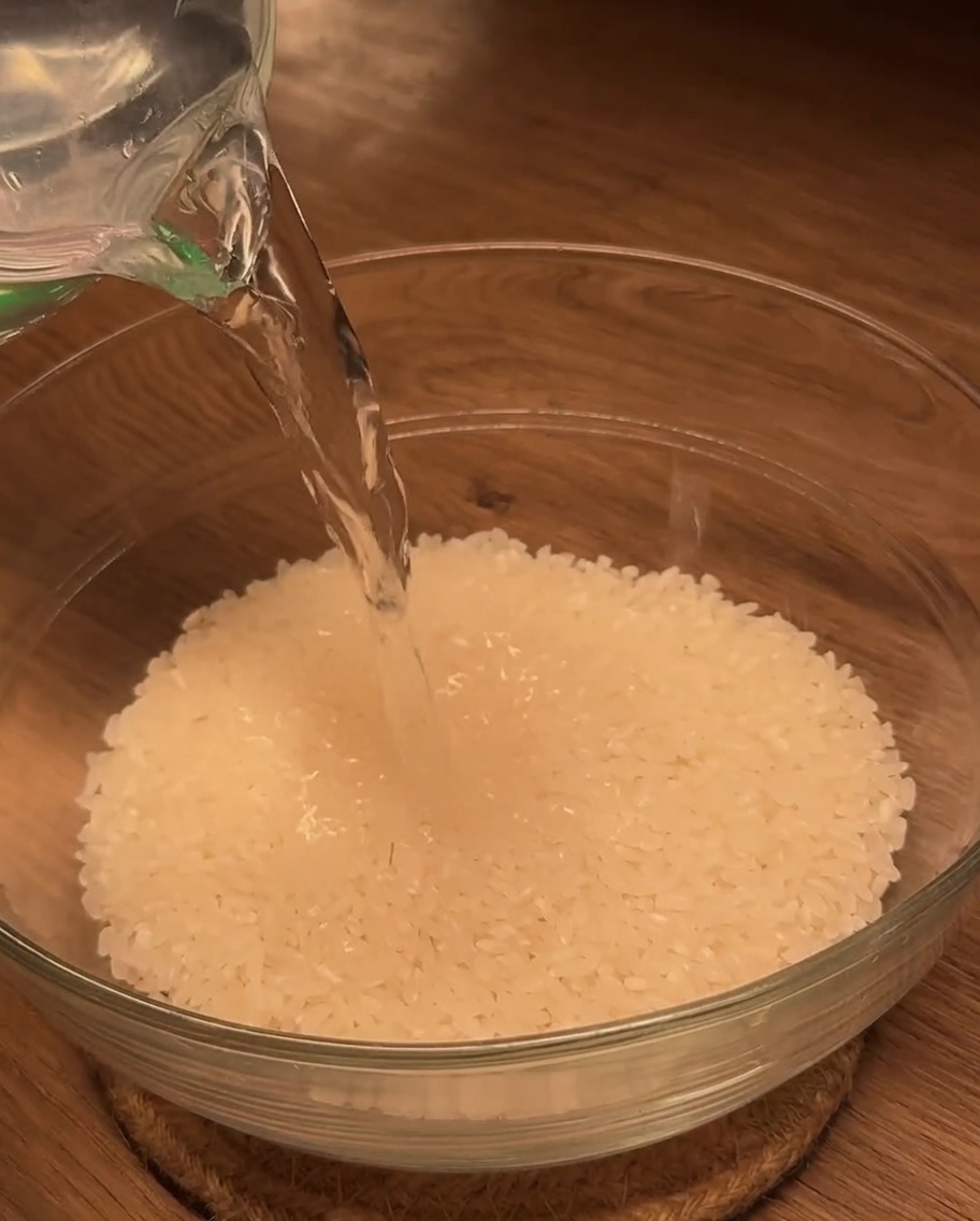 Acqua versata da un misurino in una ciotola di vetro riempita di riso bianco.