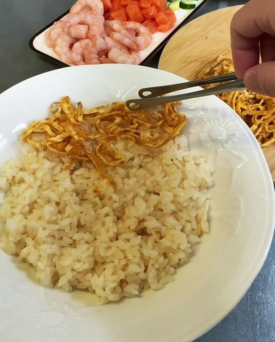 Strisce di uovo e guarnizioni di pesce distribuite sopra il riso su un piatto bianco.