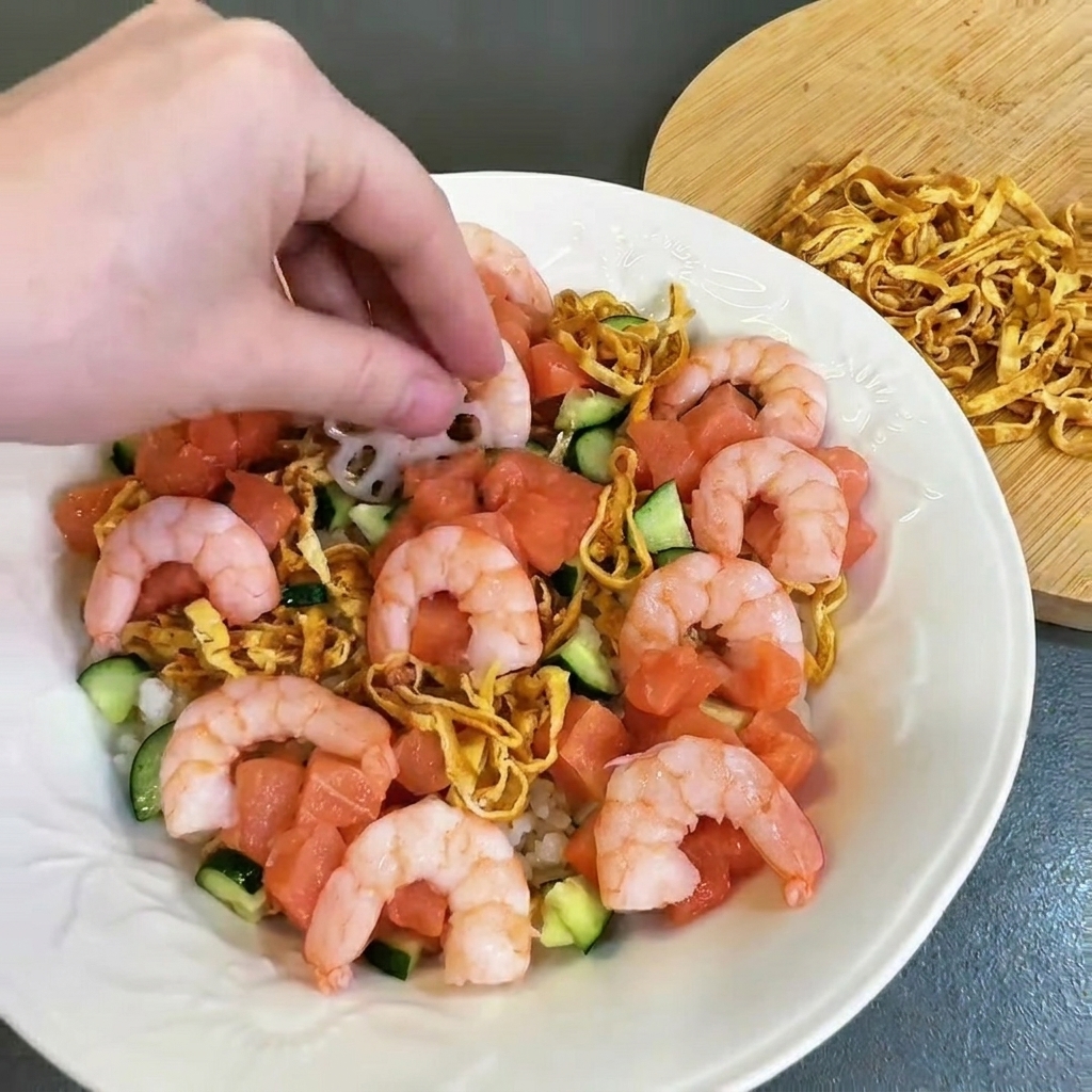 Gamberi rosa cotti disposti con cura vicino al salmone e al cetriolo.