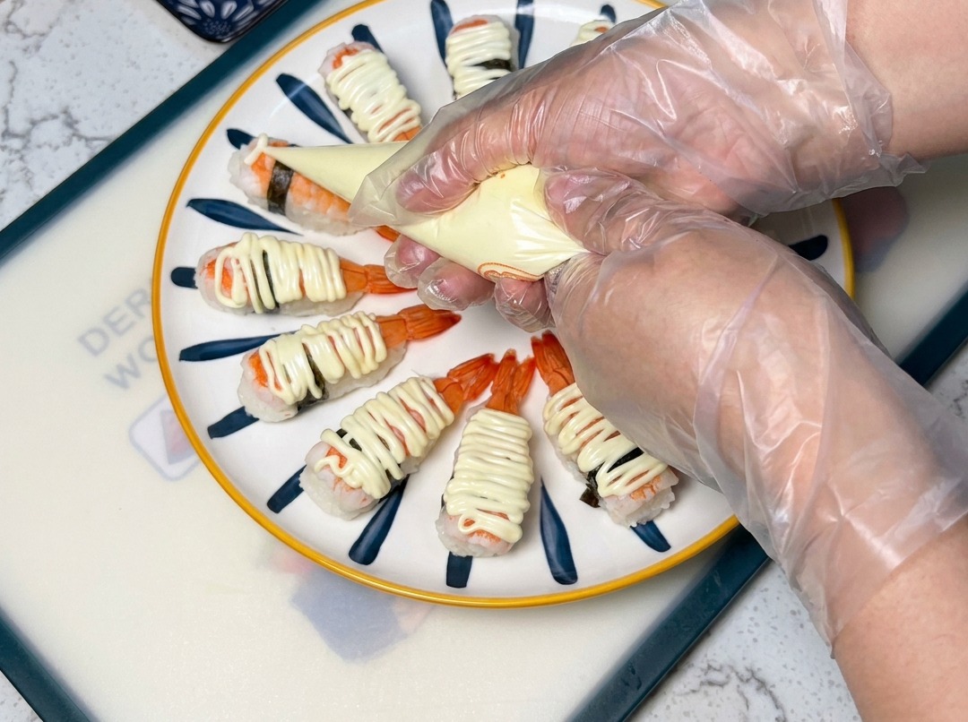 Primo piano di una sac-à-poche che distribuisce maionese sul sushi di gamberi.