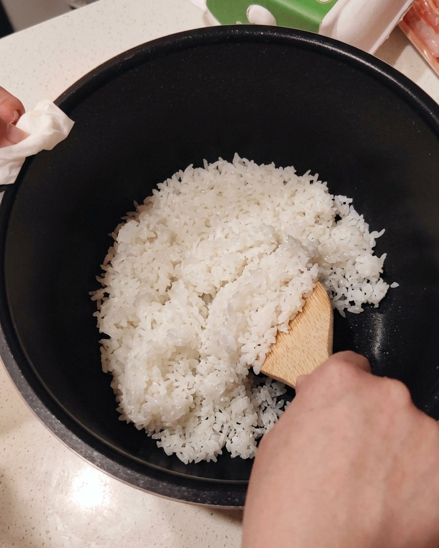 Mescolare laceto per sushi nel riso cotto caldo usando un cucchiaio di legno.