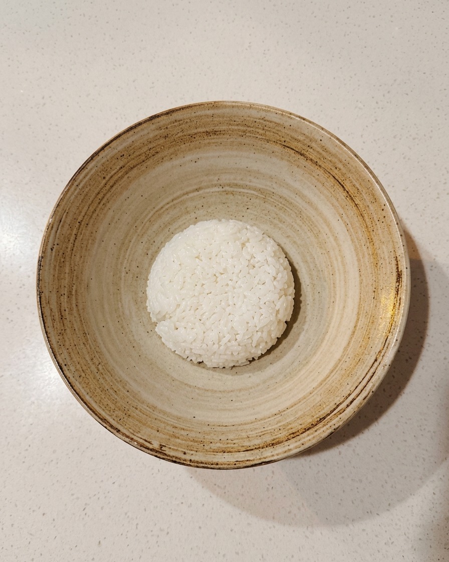 Un singolo mestolo di riso per sushi condito al centro di una ciotola di ceramica rustica.