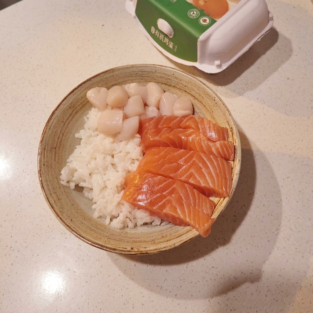Una ciotola piena di riso, guarnita con una disposizione ordinata di salmone, capesante e gamberi crudi.