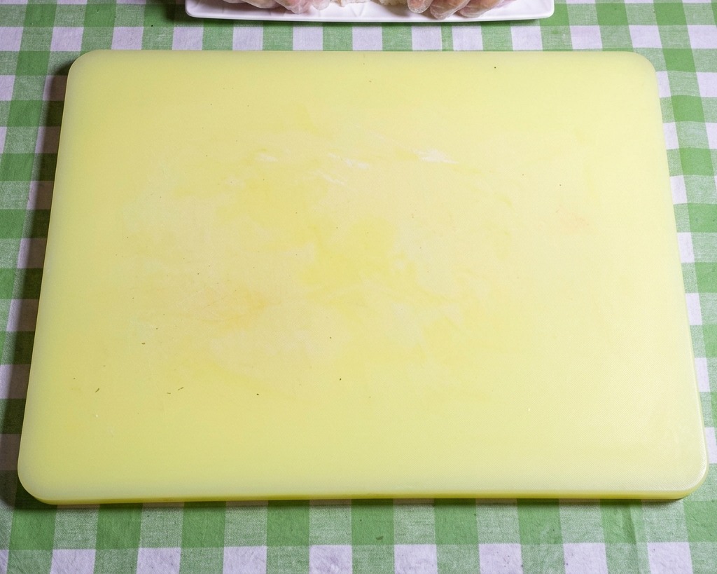 Primo piano di mani con guanti che modellano il riso appiccicoso per sushi in polpette ovali uniformi e precise su un tagliere giallo.
