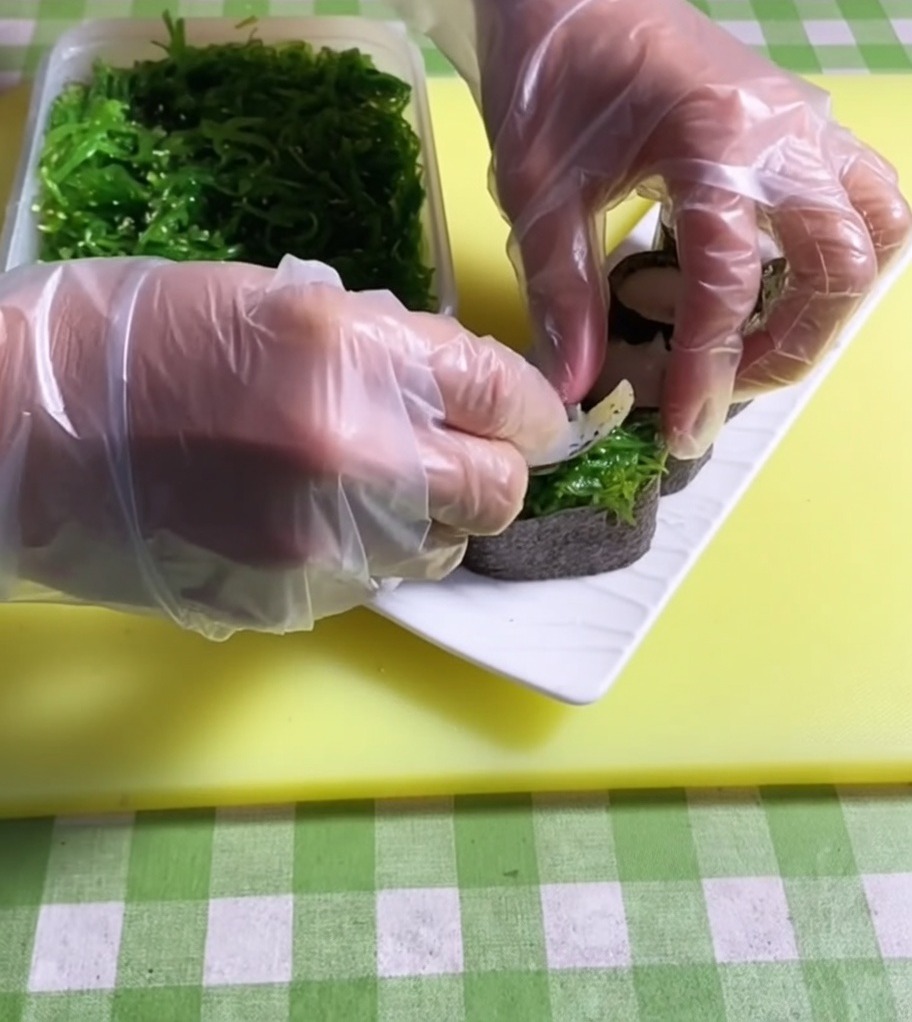 Pinzette che posizionano una porzione di insalata di alghe verde brillante sopra una base per sushi.
