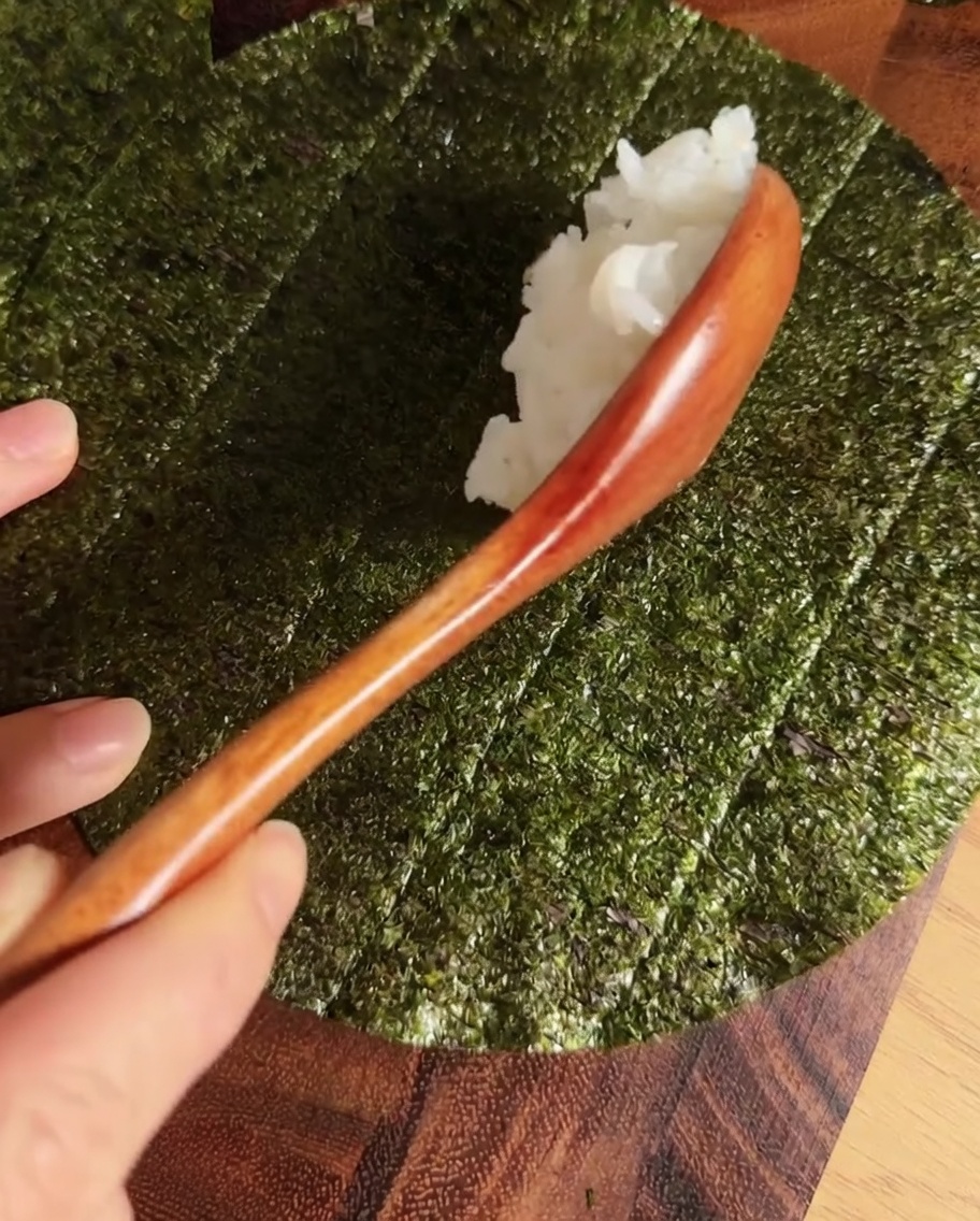 Una striscia di riso per sushi condito al centro di un foglio circolare di alga nori.