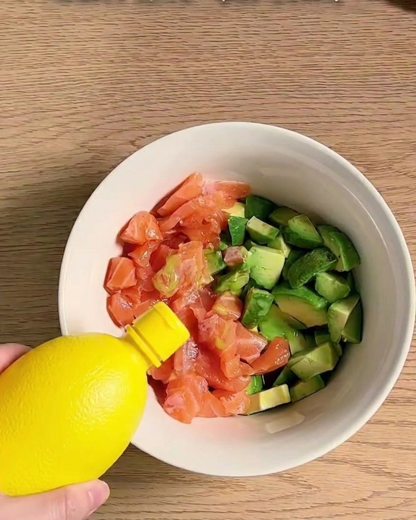 Una ciotola piena di cubetti di salmone e avocado conditi e mescolati con vari ingredienti.