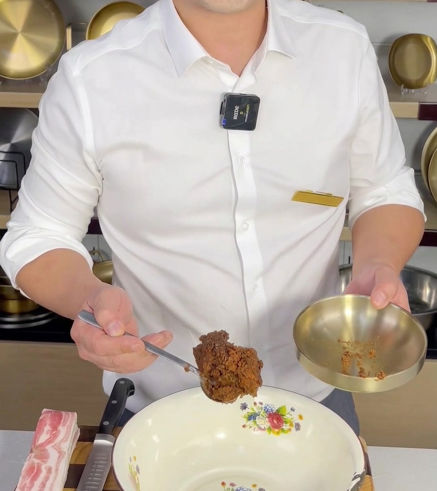 Un cucchiaio di Doenjang aggiunto a una ciotola di ceramica bianca, pronto per essere mescolato con gli altri ingredienti.