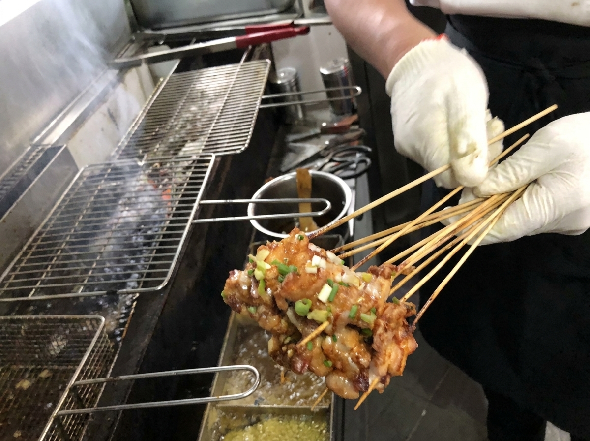 Primo piano di un pennello che applica una ricca salsa marrone su spiedini di pancetta grigliati su una griglia a carbone.