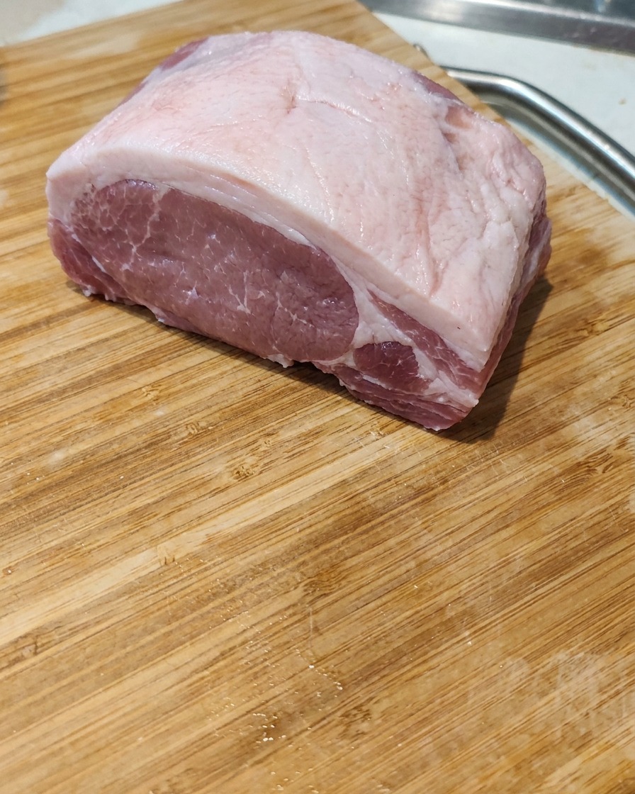 Primo piano di un trancio di pancia di maiale cruda tagliata a fette spesse e regolari su un tagliere di legno.