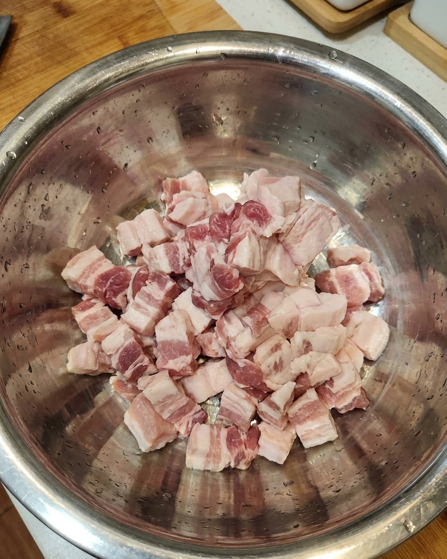 Fette di pancia di maiale cruda riunite in una grande ciotola in acciaio inossidabile.