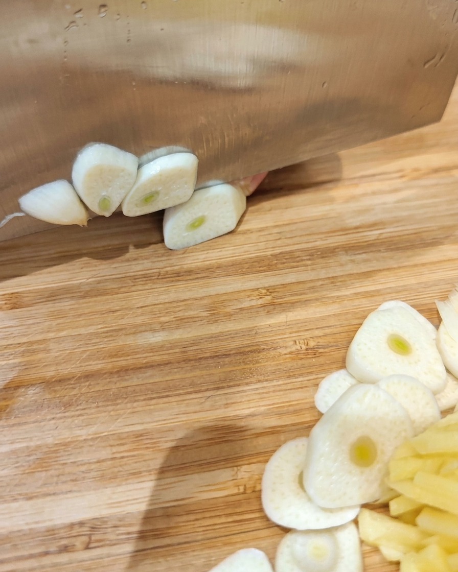Pancia di maiale cruda in una ciotola con fette di aglio, zenzero e varie spezie in polvere.