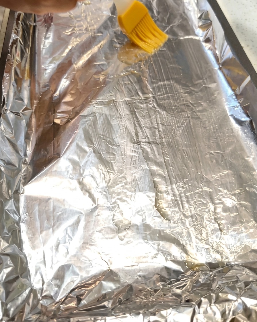 Un pennello spande olio su un foglio di alluminio allinterno di una teglia da forno.