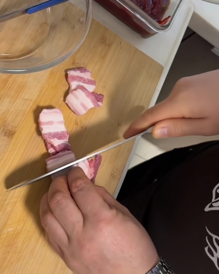 Fette spesse di pancetta fresca con cotenna disposte su un tagliere di legno accanto a un coltello.