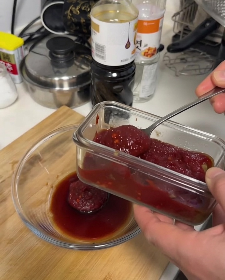 Una salsa rosso scuro densa mescolata con un cucchiaio in una ciotola di vetro trasparente su una superficie in legno.