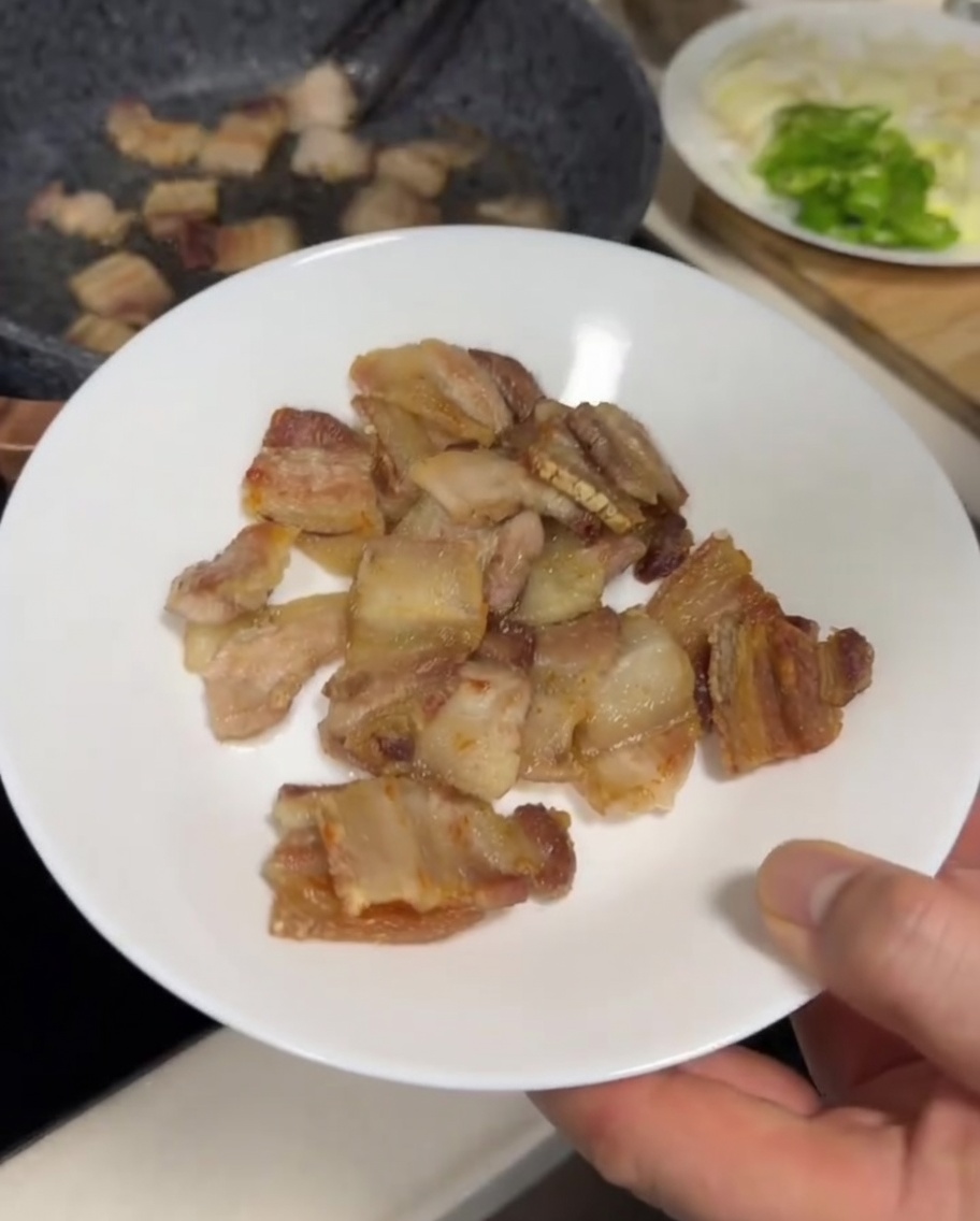 Fette di pancetta che friggono in una padella grigia, mostrando un esterno dorato e leggermente croccante.