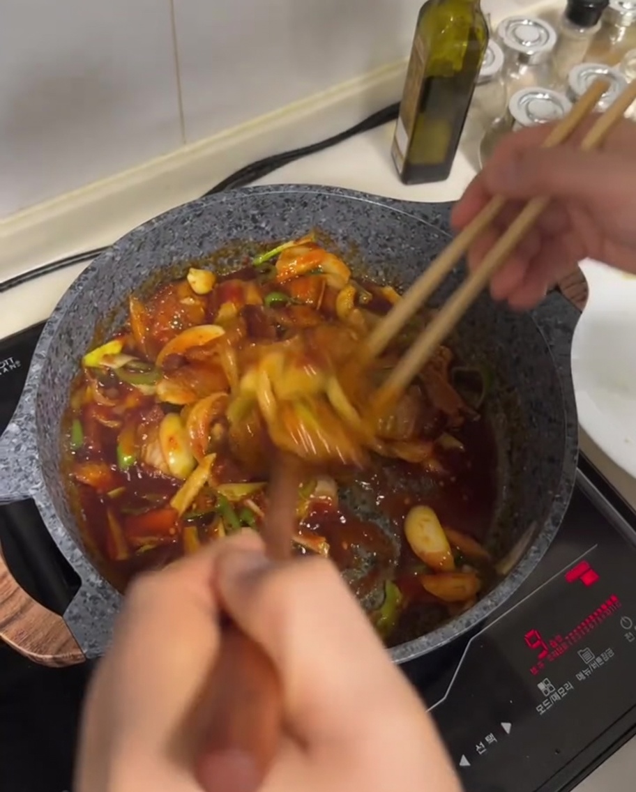 Pancetta e verdure saltate mescolate in una salsa rossa in una padella.