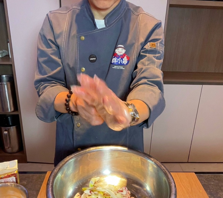 Chef che indossa un guanto trasparente mescola la pancetta cruda e gli aromi in una ciotola di metallo.