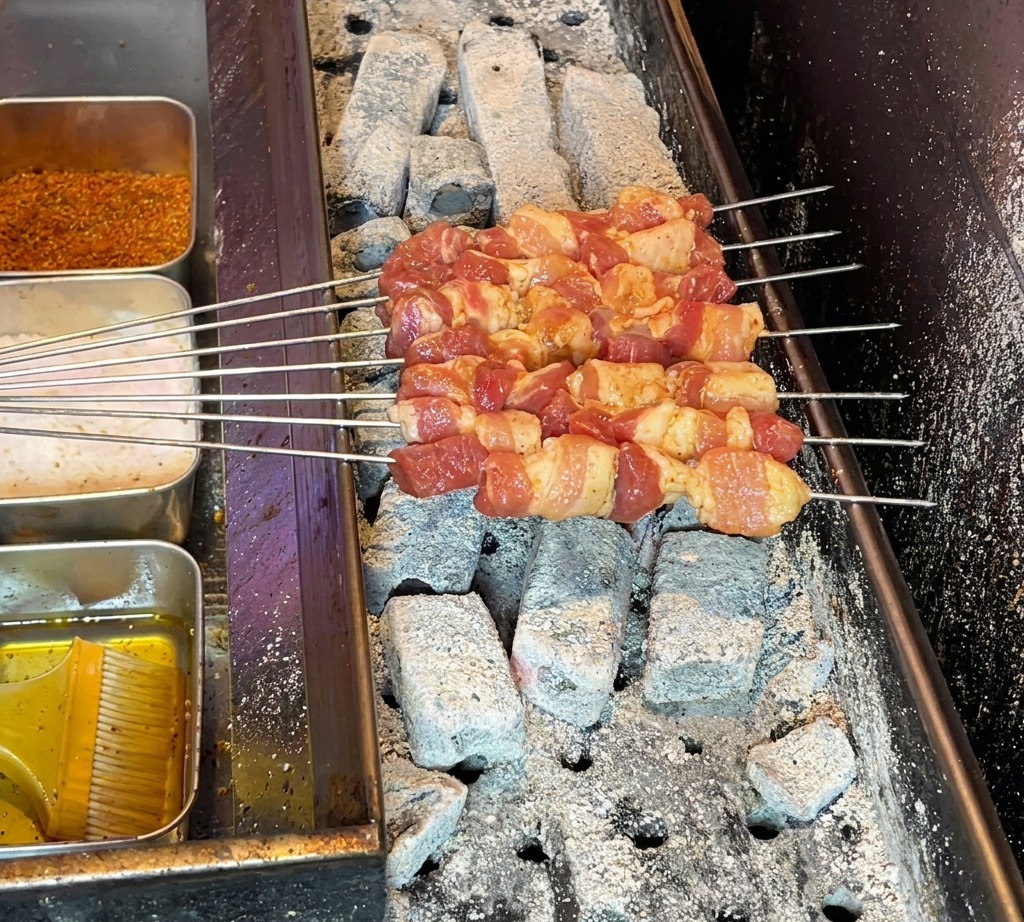 Spiedini di pancetta crudi sistemati su una griglia a carbone ardente, pronti per la cottura.