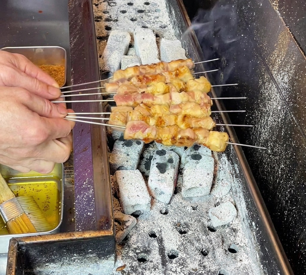 Le mani dello chef muovono con cura gli spiedini per garantire una distribuzione uniforme del grasso sulla carne in cottura.