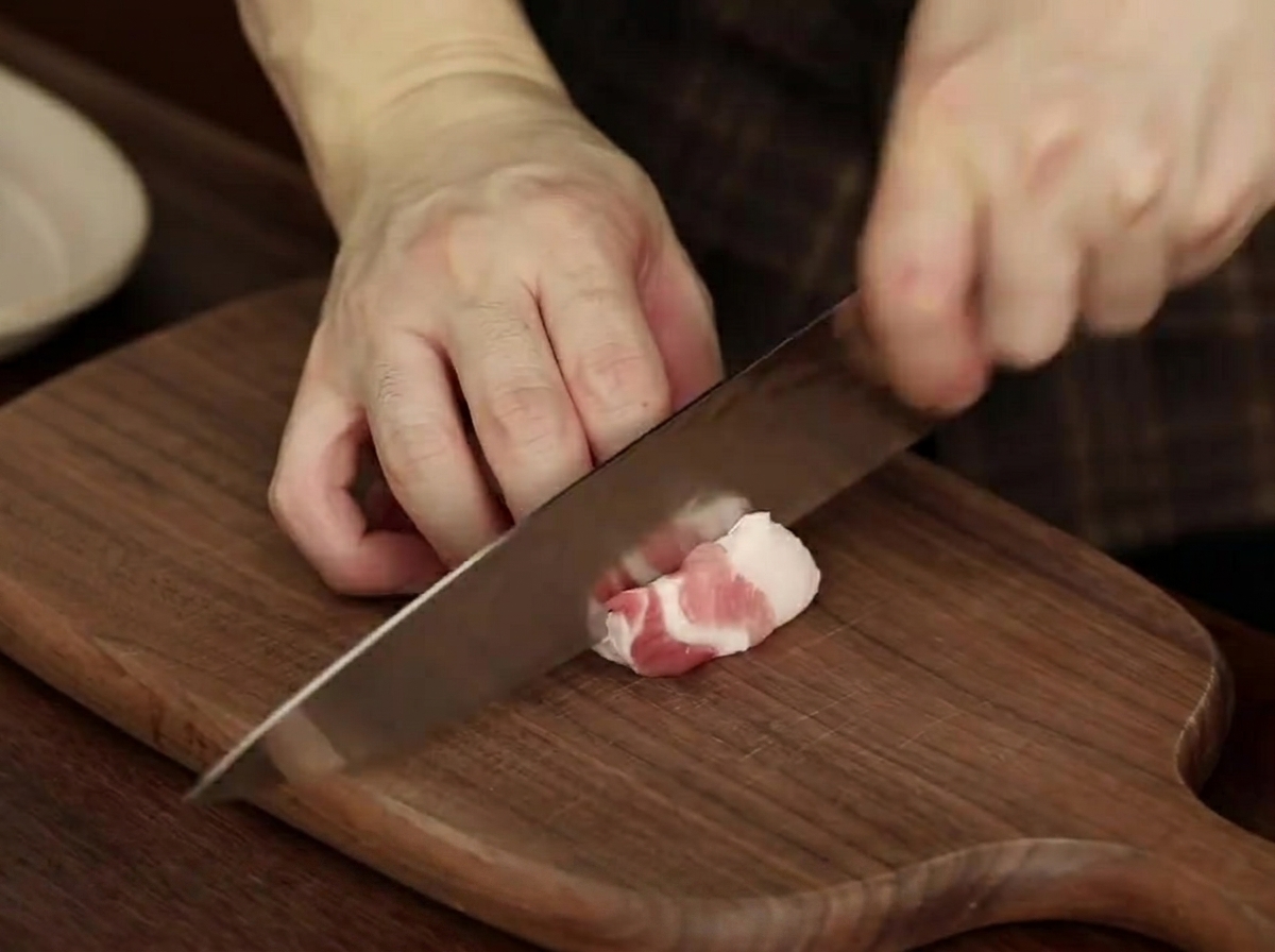 Fette di pancetta di maiale cruda disposte ordinatamente su un piatto, pronte per lo stufato.