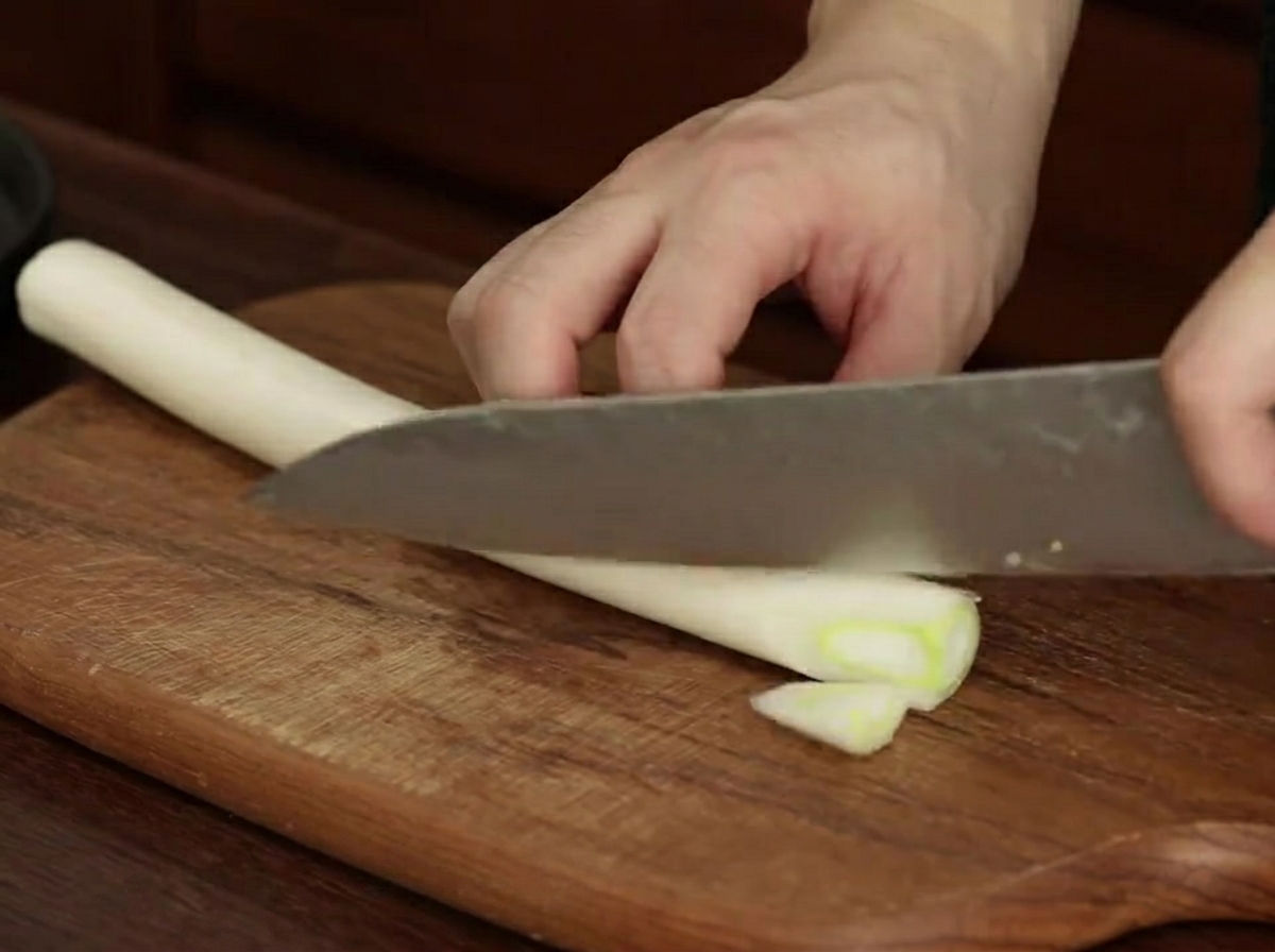 Pezzi di porro tagliati diagonalmente su un tagliere di legno.