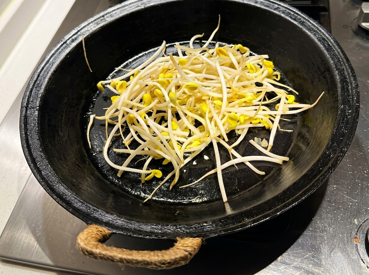 Germogli di soia freschi e puliti sparsi in una padella nera preriscaldata e oliata.