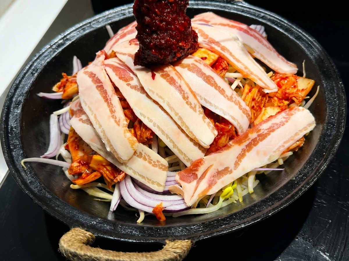 Una salsa vibrante per stir-fry coreano rosso distribuita sopra una padella di pancetta a strati e verdure fresche.