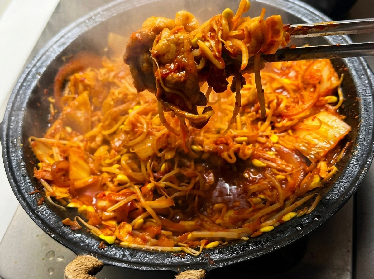 Il mix di pancetta al kimchi con germogli di soia mescolato nella padella su una fiamma alta.