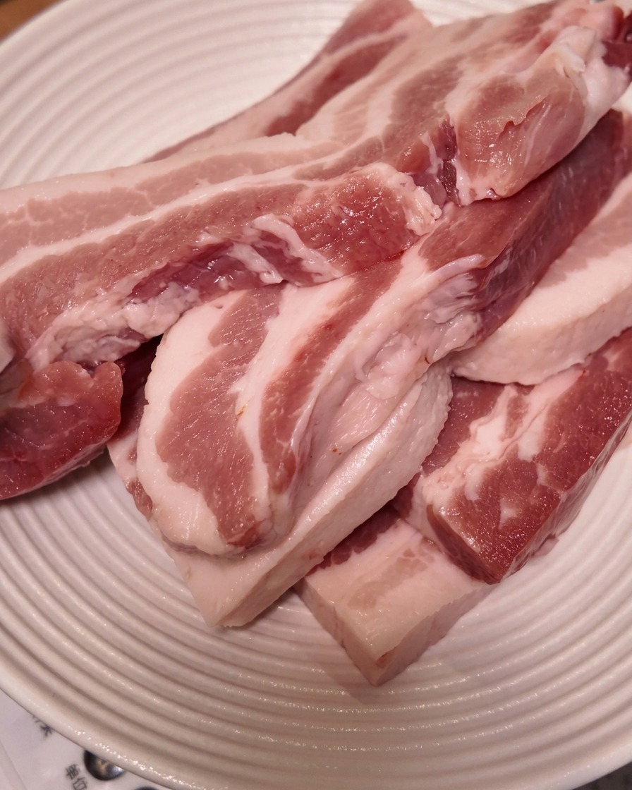 Fette spesse di pancetta cruda impilate su un piatto bianco rigato.