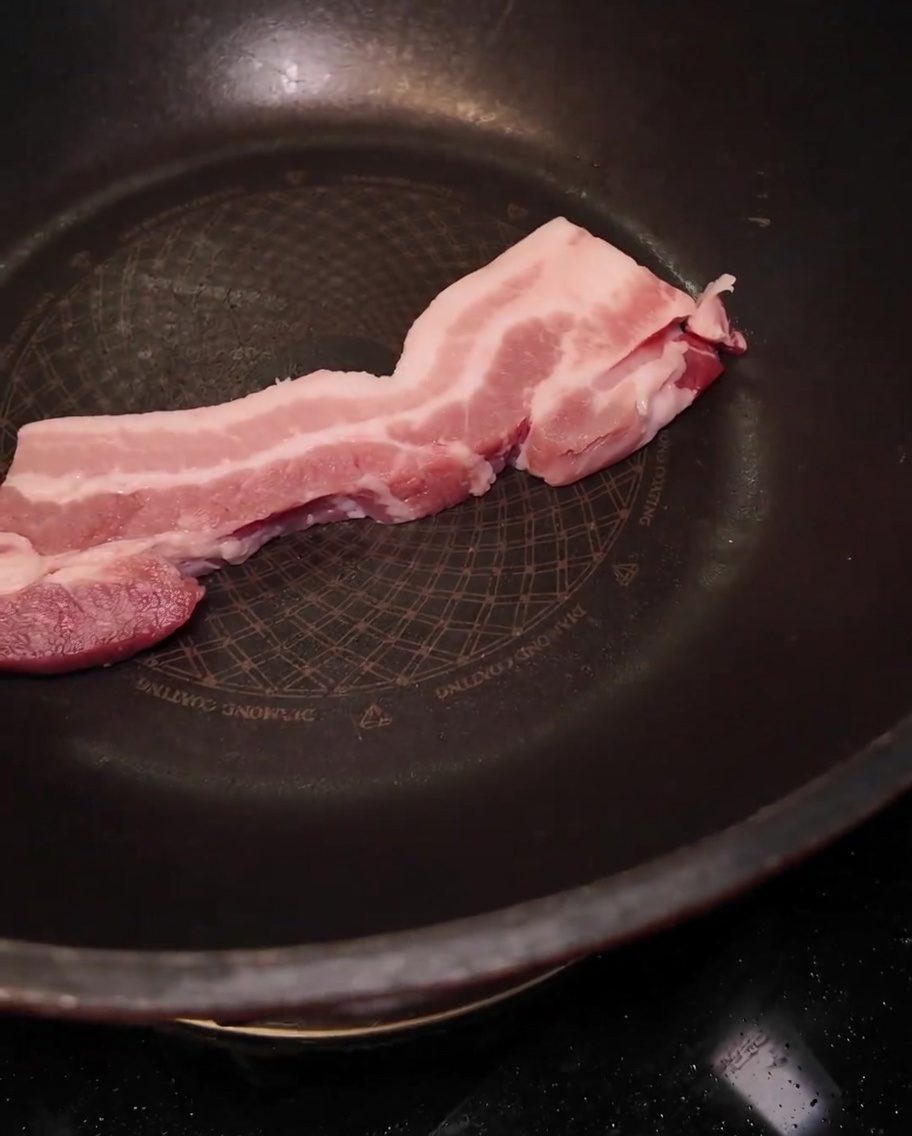 Una fetta spessa di pancetta cruda posizionata in una grande padella nera.