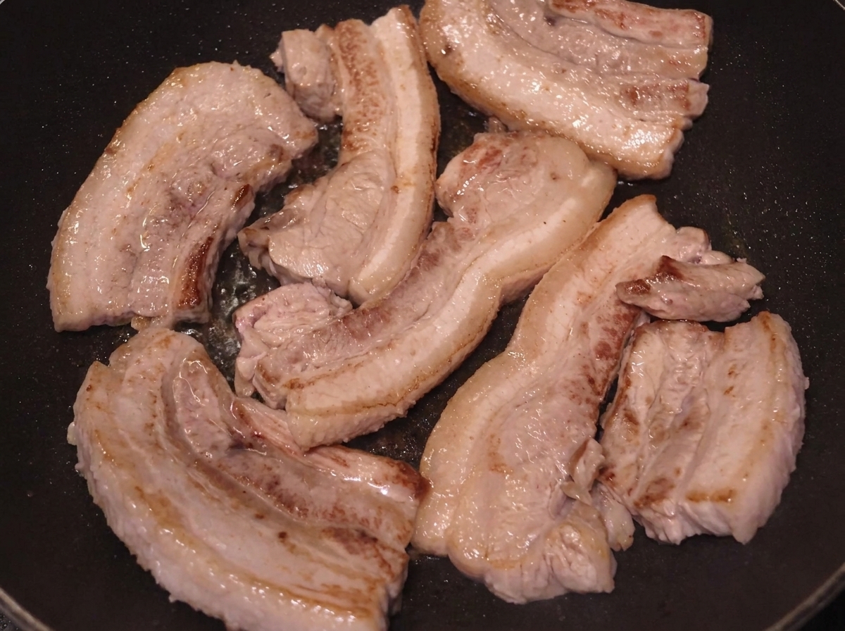 Diverse fette di pancetta rosolate in padella con le superfici ben dorate.