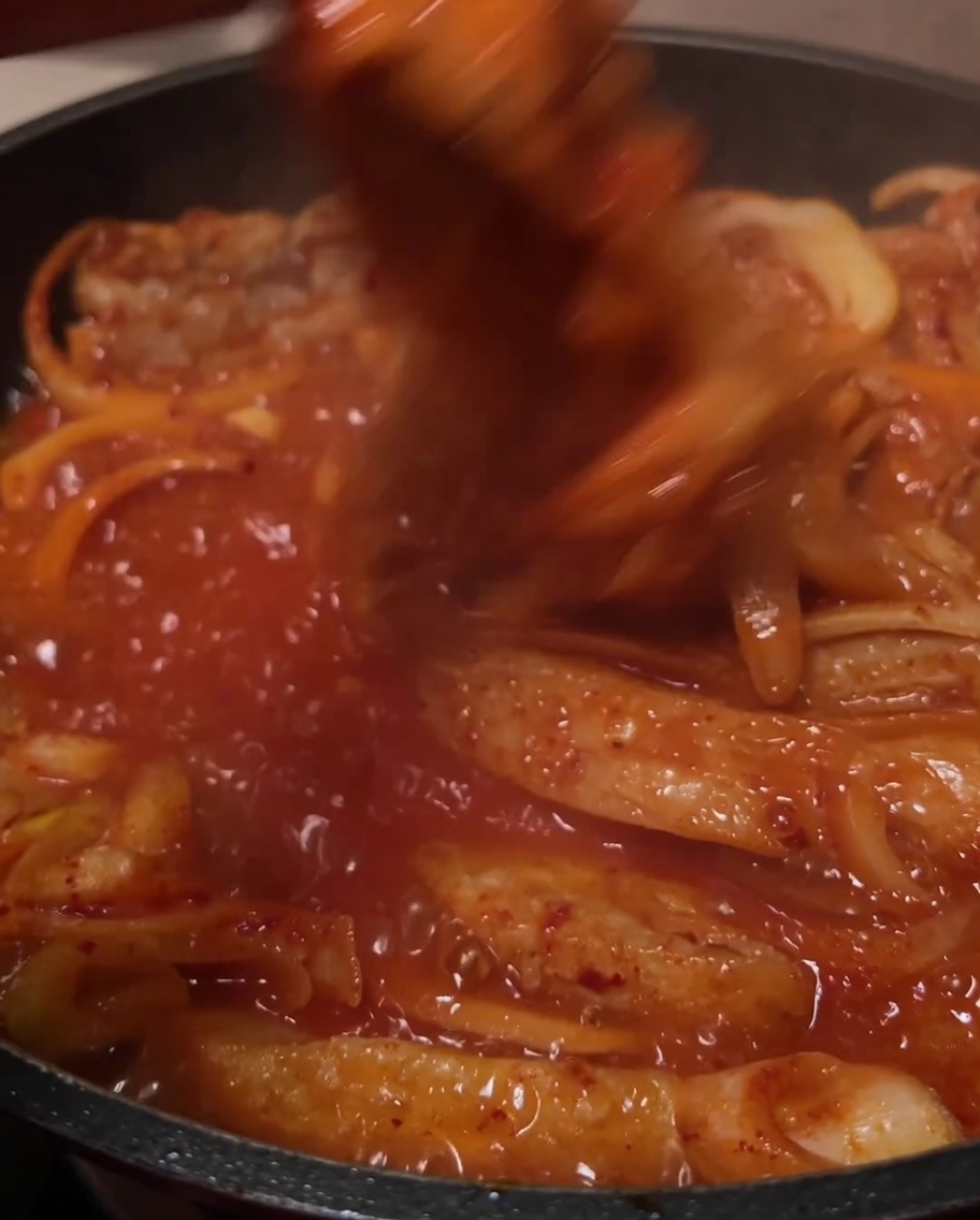 Gli ingredienti mescolati insieme nella salsa rossa che bolle in padella.