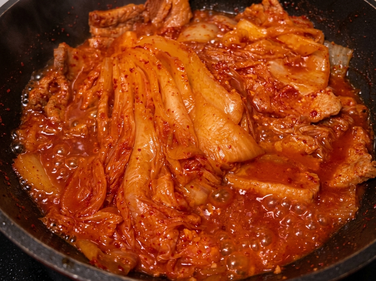 Olio versato da un cucchiaio nella padella con il maiale e il kimchi brasati.