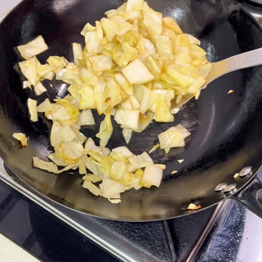 Pezzi di crauti sollevati da un wok caldo con una spatola di metallo.