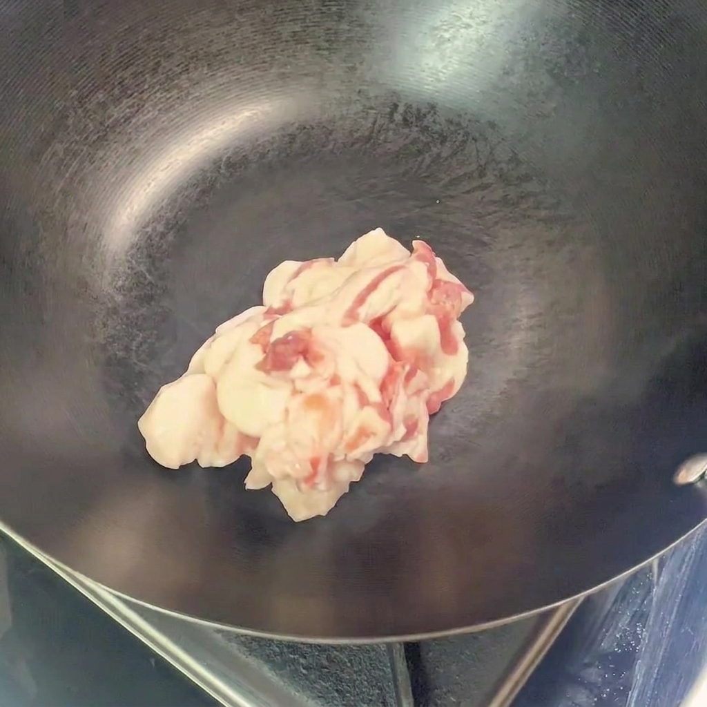 Un mucchio di pezzi di pancetta di maiale cruda affettata posta al centro di un wok vuoto e preriscaldato.