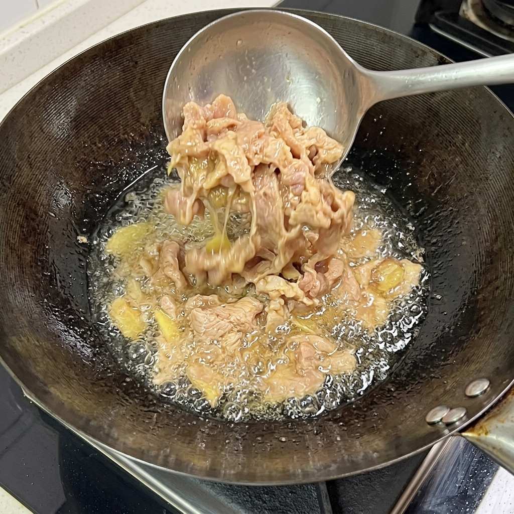 Fette di maiale che friggono nel wok, mostrando una superficie cotta e dorata.